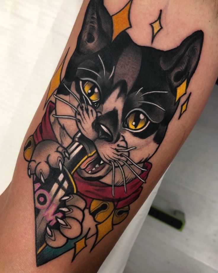 a black and white cat with yellow eyes holding a knife in its mouth tattoo on the arm