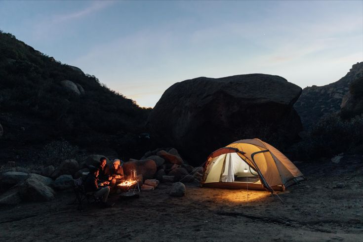 a tent set up next to a campfire on a rocky hillside at night with the lights on