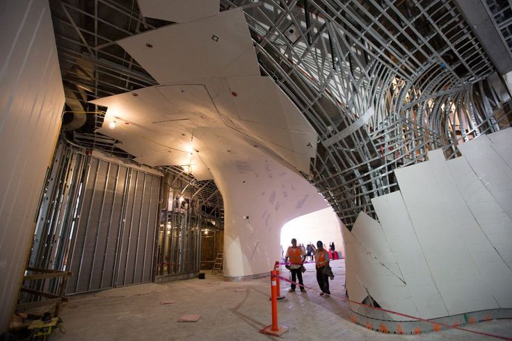 some people are walking around in a large room with metal structures on the ceiling and walls