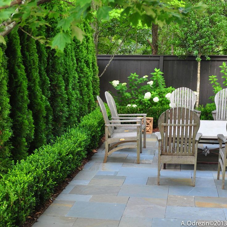 an outdoor patio with chairs and table surrounded by greenery