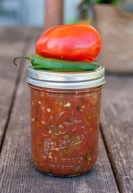 a jar filled with pickles and tomatoes on top of a wooden table