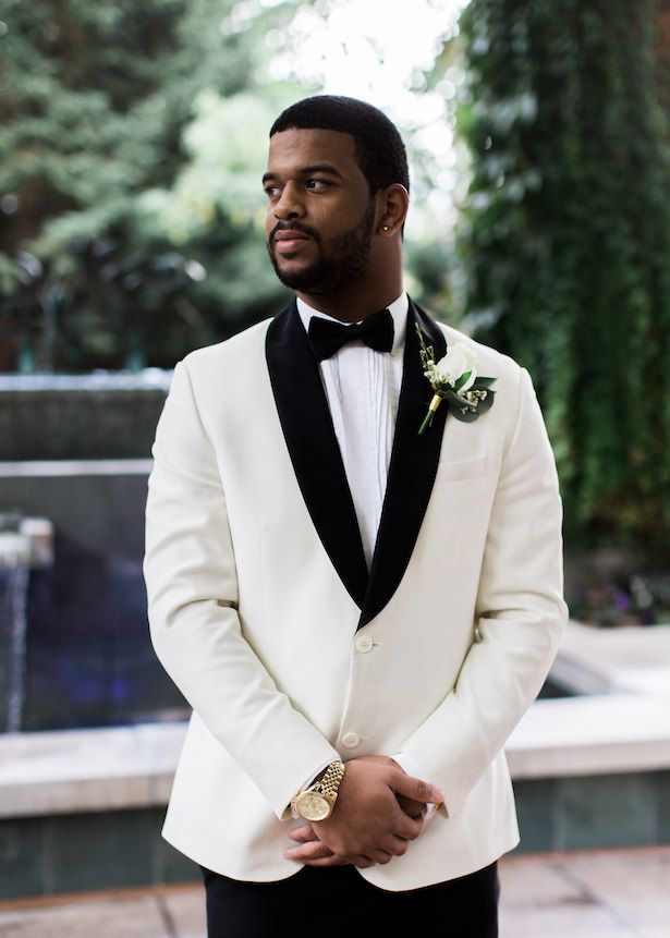 a man in a white tuxedo standing next to a fountain