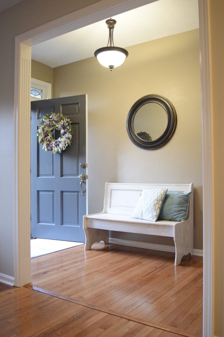 a white bench sitting on top of a hard wood floor next to a blue door