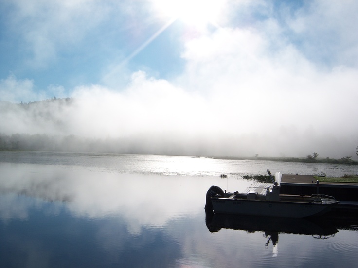 a boat sitting on top of a lake next to a dock covered in fog and low lying clouds