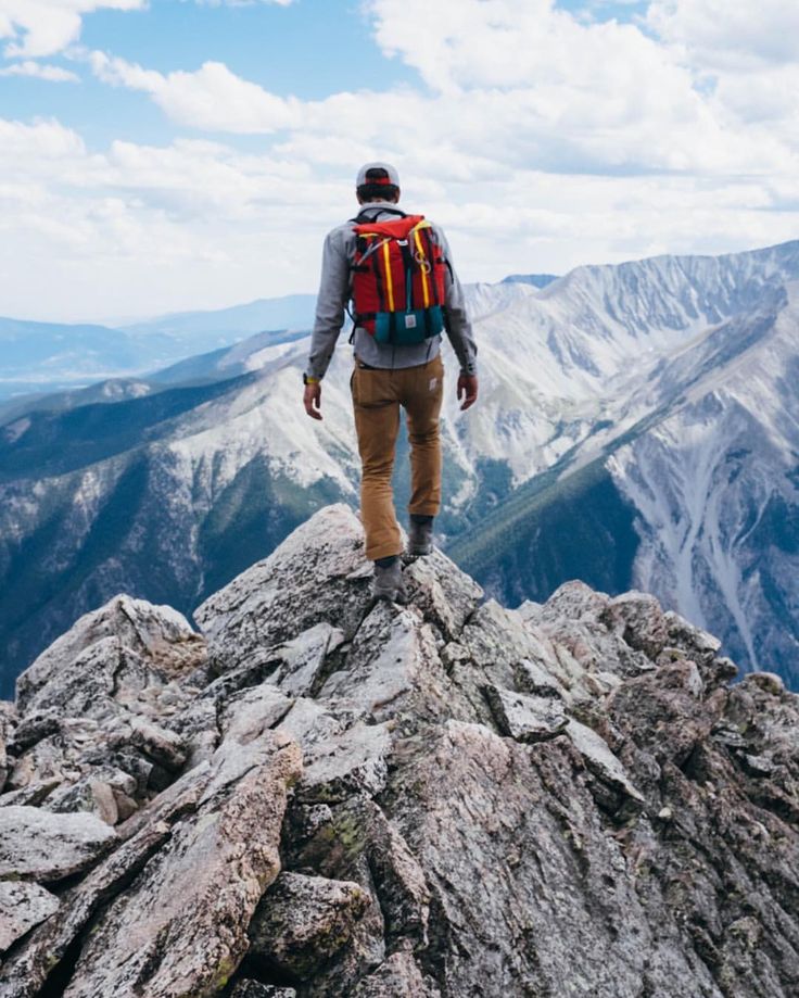 a man with a backpack is standing on top of a mountain looking at the mountains