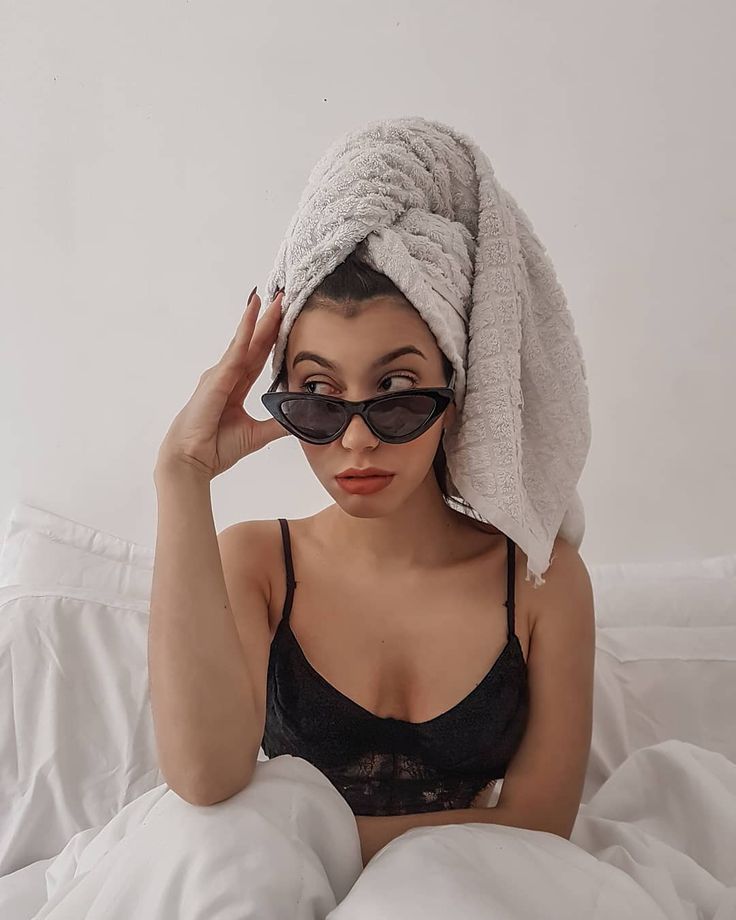 a woman wearing sunglasses and a towel on her head sitting in bed with white sheets