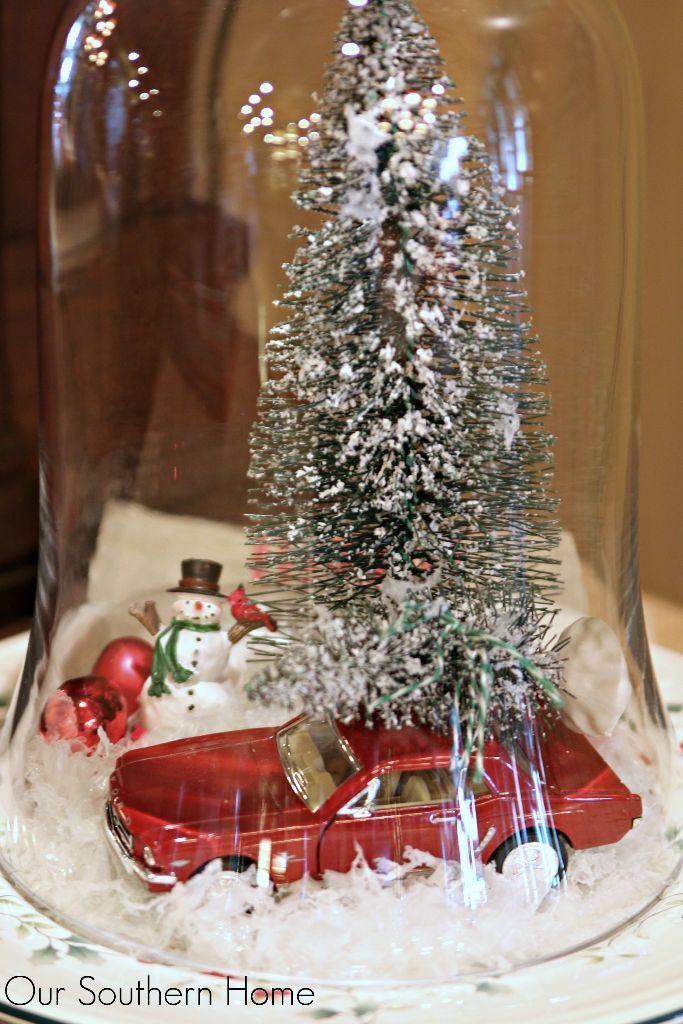 a christmas tree under a glass clochet on a plate with snow around it