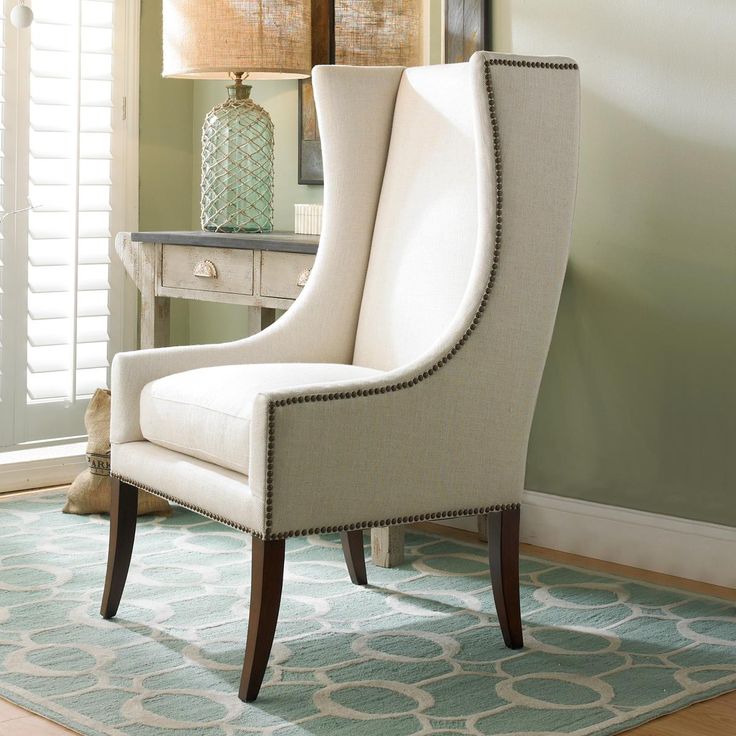 a white chair sitting on top of a rug in front of a table with a lamp