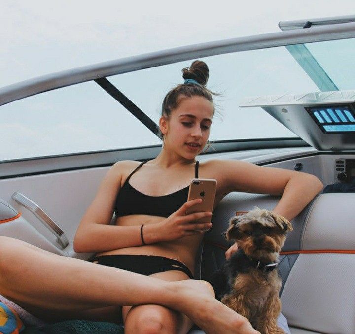 a woman sitting in the back seat of a boat with her dog looking at an electronic device