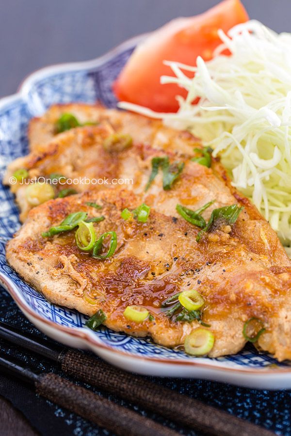 two pieces of fish on a blue and white plate with shredded cheese, tomatoes and green peppers