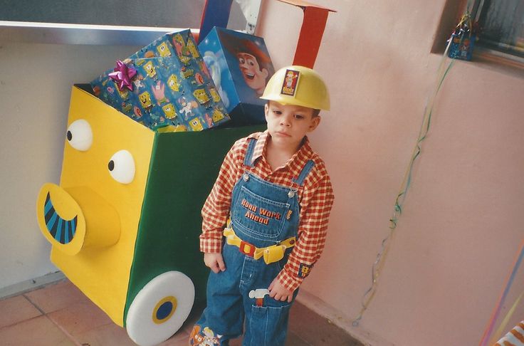 a young boy wearing overalls and a hard hat standing next to a cardboard box