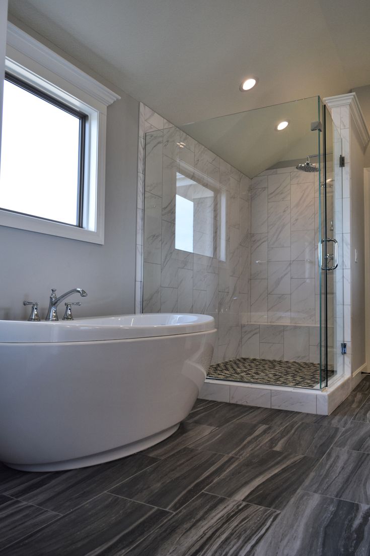 a white bath tub sitting next to a walk in shower under a bathroom window on top of a hard wood floor