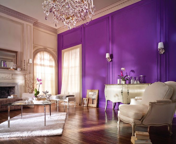 an elegant living room with purple walls and white furniture, chandelier above the fireplace