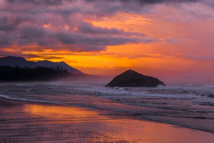 the sun is setting over an ocean with mountains in the distance and water on the beach