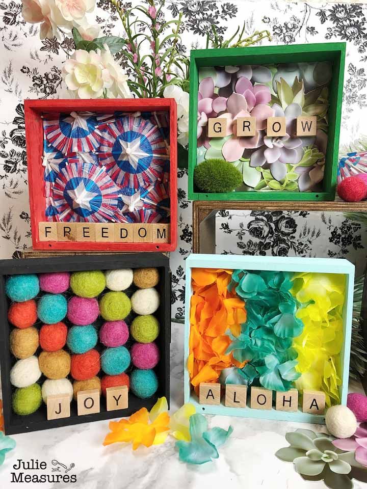 three boxes with different types of flowers and words in them on a table next to wallpaper