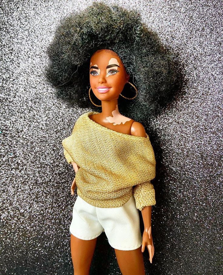 a doll with an afro standing next to a black wall and wearing a yellow sweater