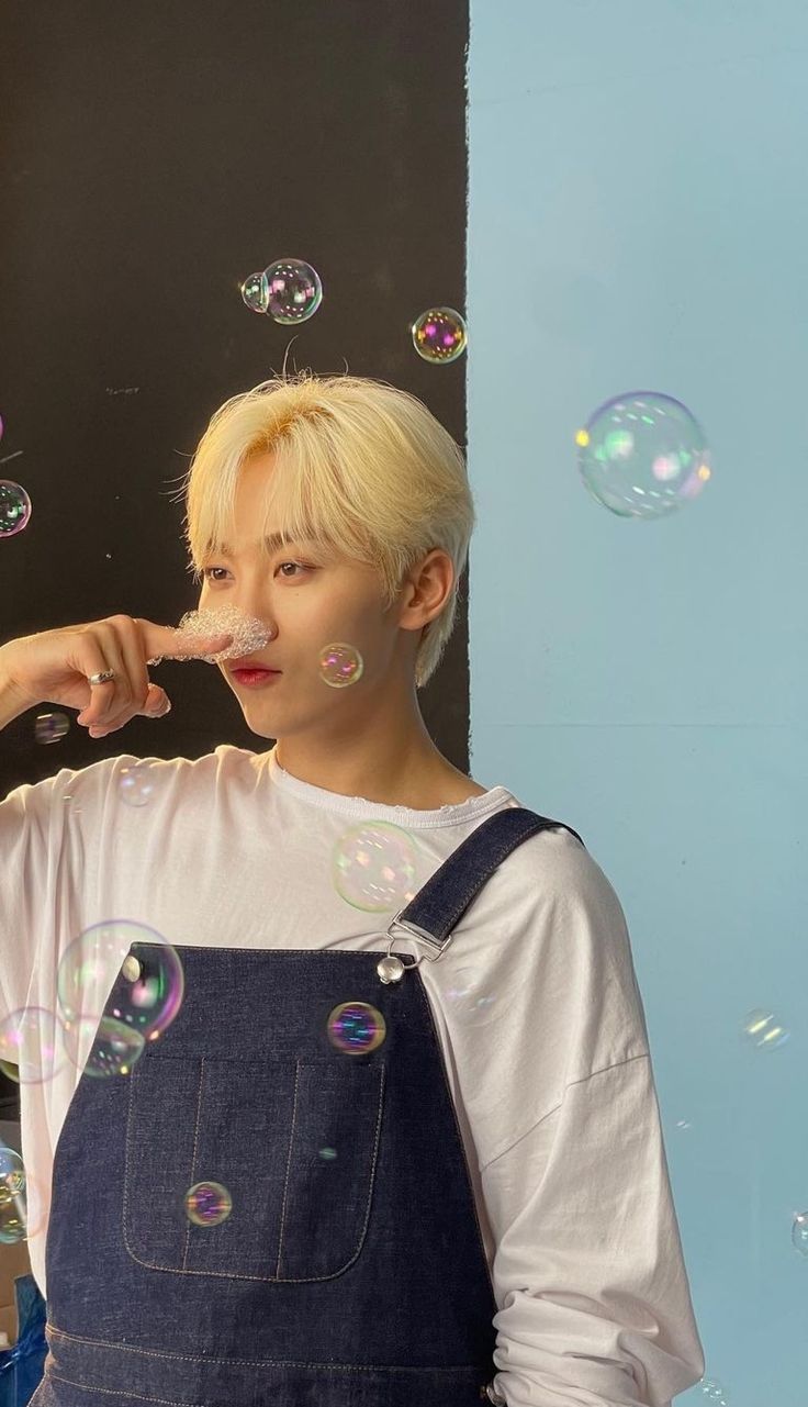 a person with blonde hair and overalls is blowing soap bubbles in front of them