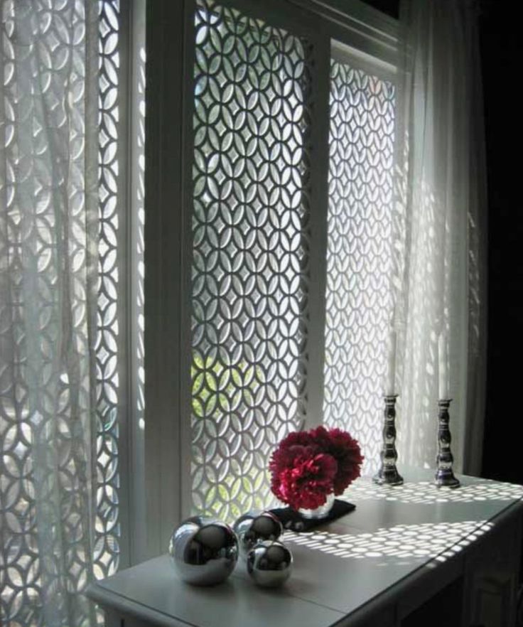 a vase with flowers sitting on top of a table next to a window covered in sheer curtains