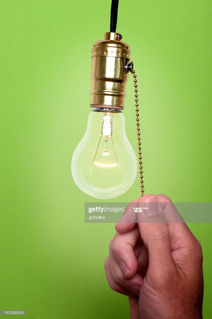 a hand holding a light bulb with a chain hanging from it's end on a green background