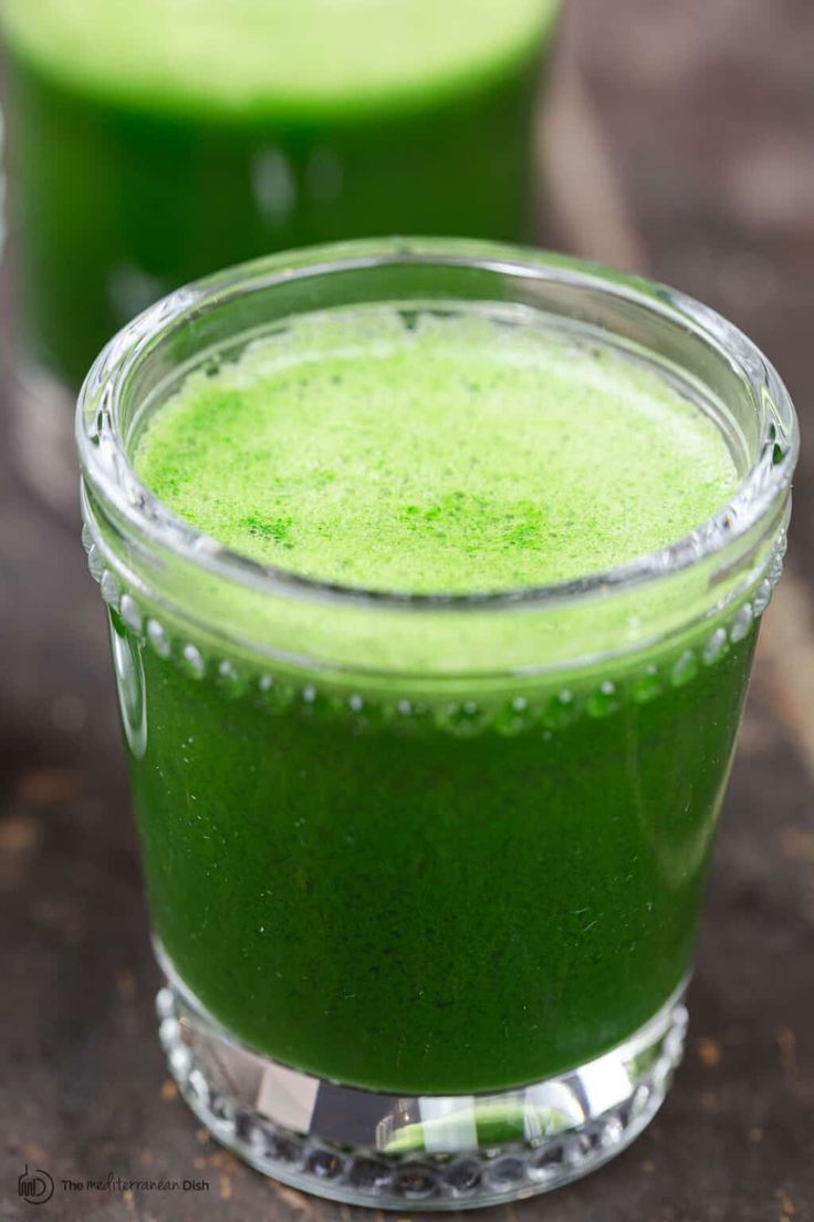 two glasses filled with green liquid on top of a table