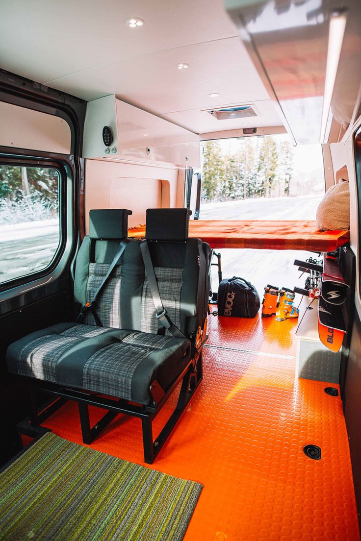 the interior of a camper van with orange flooring and black seats on it