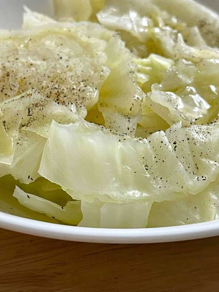 a white bowl filled with cabbage covered in seasoning on top of a wooden table