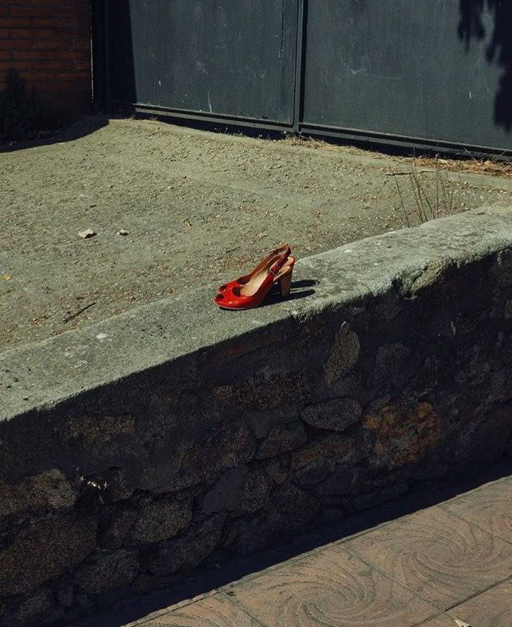 a pair of red shoes sitting on top of a stone wall