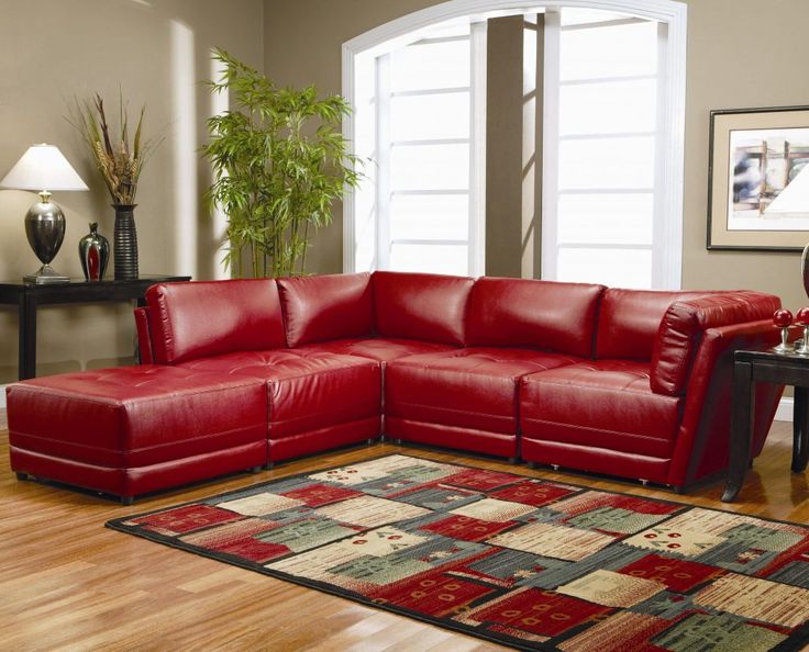 a red leather sectional sofa sitting on top of a wooden floor next to a table