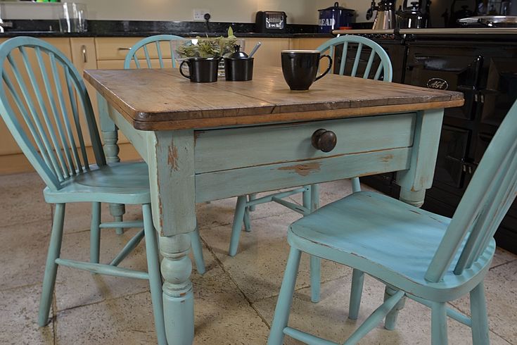 an old kitchen table with two chairs and a coffee mug on it, in front of the counter