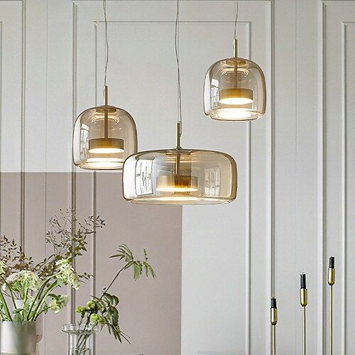 a dining room table with four lights hanging from it's ceiling and two vases filled with flowers