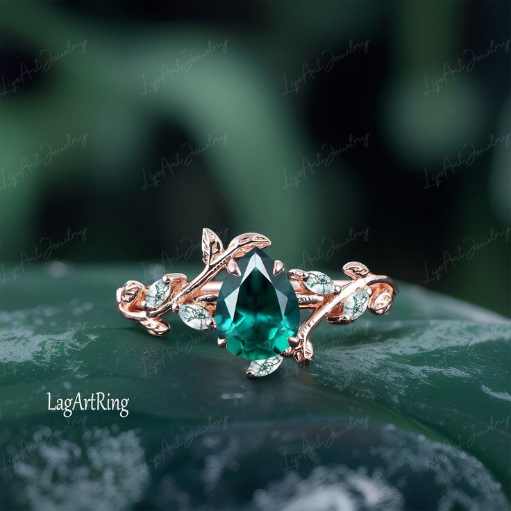 an emerald colored ring with leaves on it's side, sitting on top of a leafy green surface