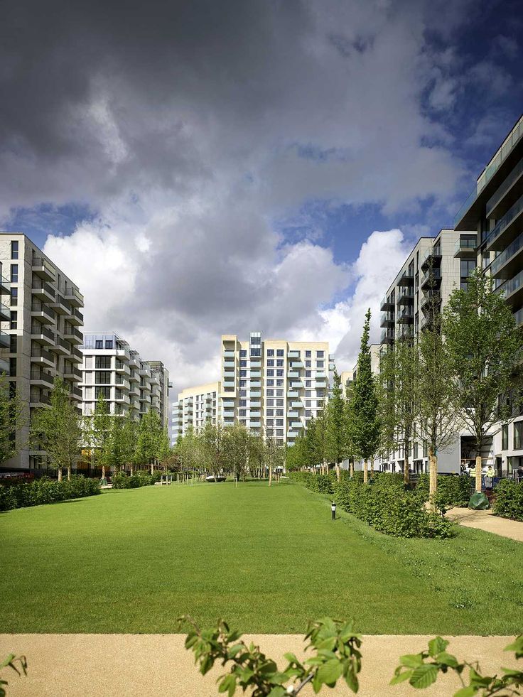 an empty grassy field in front of apartment buildings on a cloudy day with dark clouds overhead