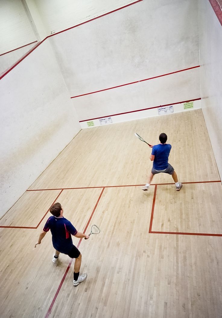 two men are playing tennis in an indoor court with red lines on the wood floor