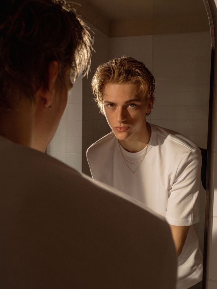 a young man is looking at himself in the mirror while he looks into the mirror