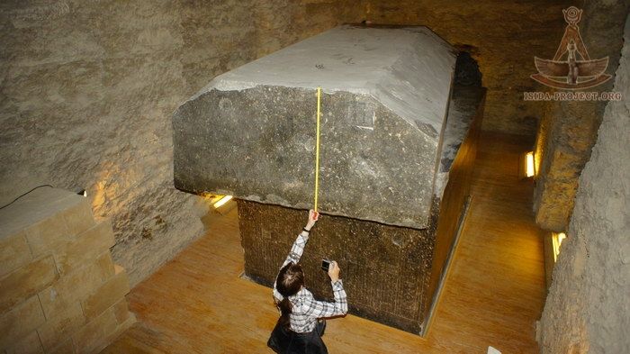 a woman measuring the height of a large rock in a room with stone walls and wooden floors