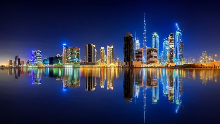 the city is lit up at night with its lights reflecting in the water and skyscrapers