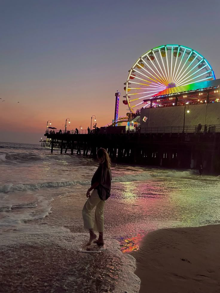 a woman walking on the beach next to a ferris wheel