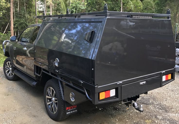 the back end of a black truck parked on a dirt road in front of trees