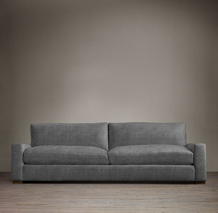 a gray couch sitting on top of a wooden floor next to a wall with a light brown background