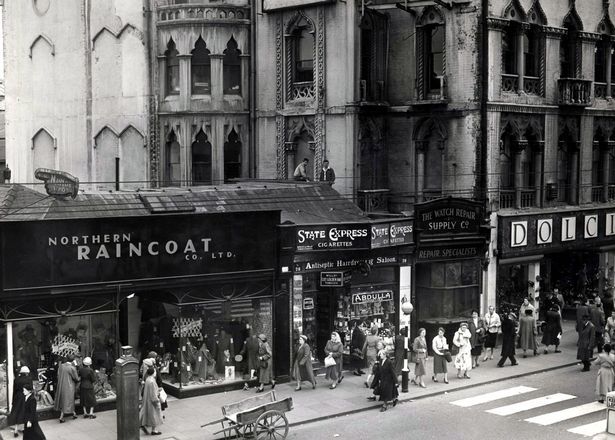 an old black and white photo of people walking down the street in front of stores