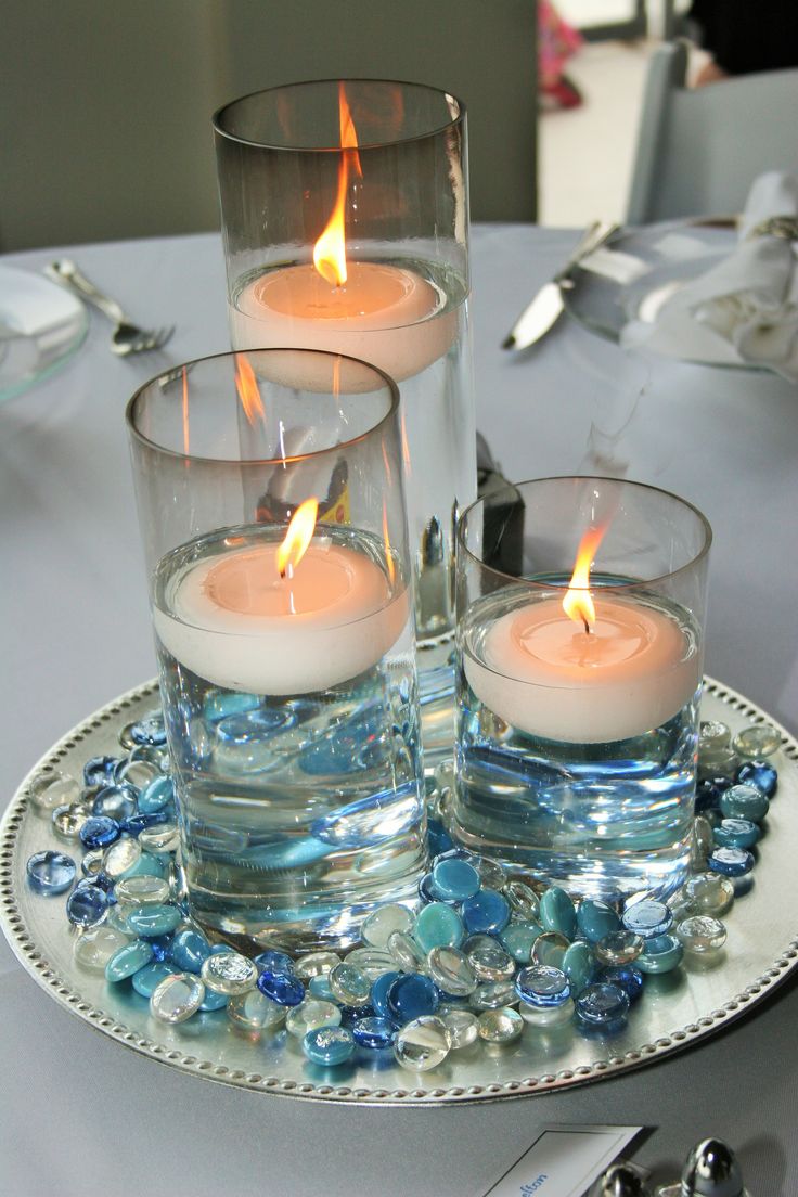 three candles are sitting on a plate with blue glass beads and water in it, surrounded by silverware