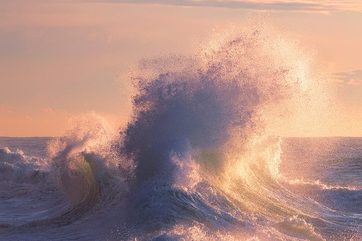 a large wave crashing into the ocean at sunset