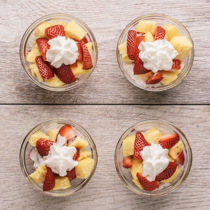 four small glass bowls filled with fruit on top of a wooden table and topped with whipped cream