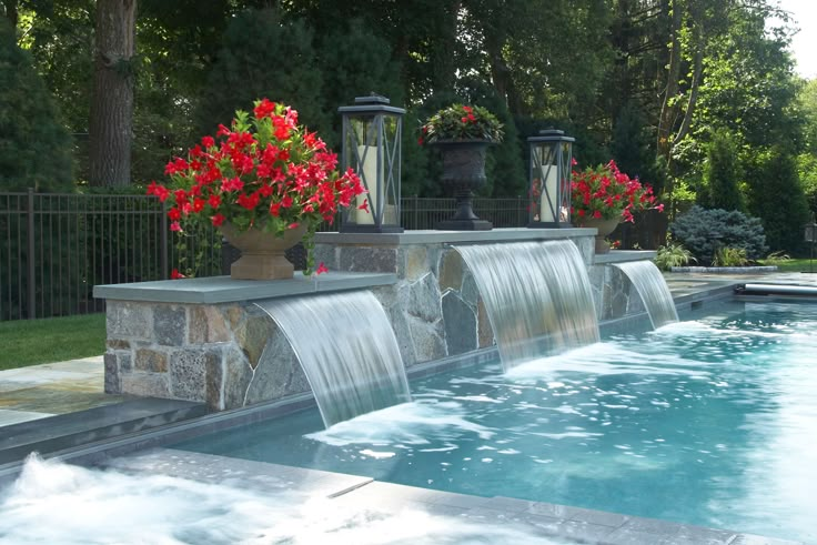 an outdoor pool with waterfall and red flowers