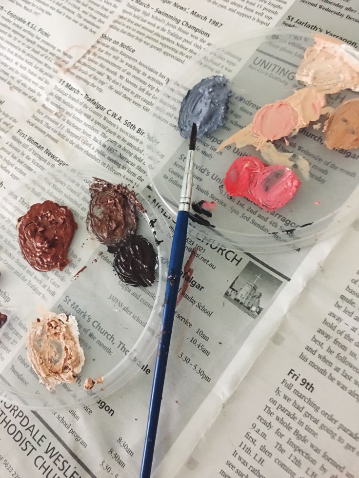 an artist's palette with paint and brushes on top of newspaper