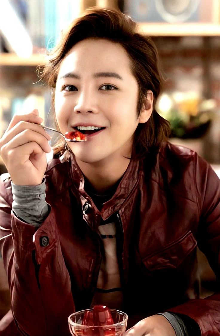 a woman eating food from a bowl with a spoon in her mouth and smiling at the camera