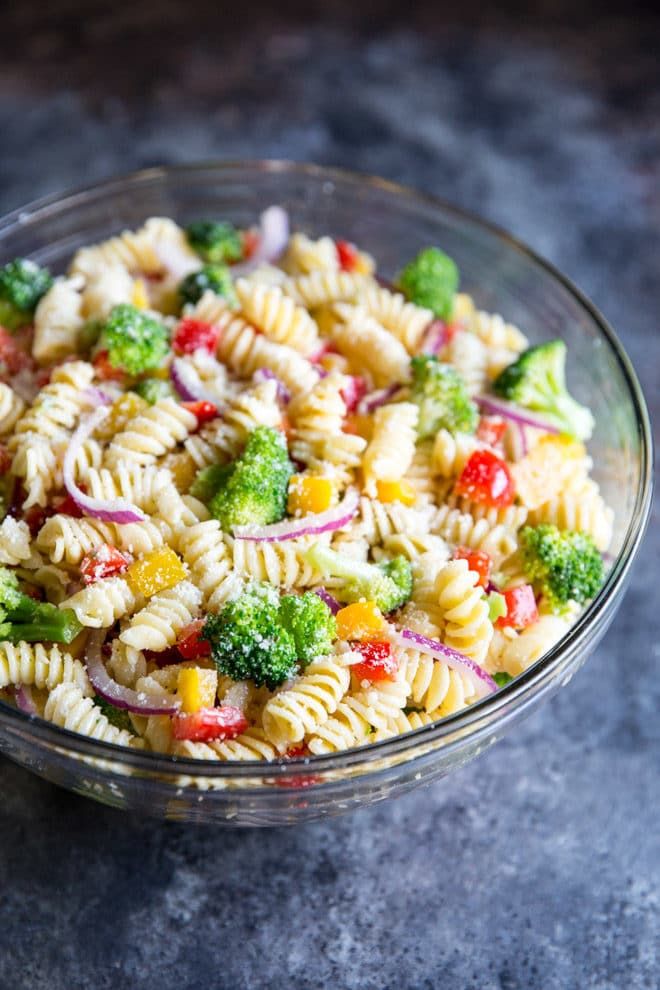 pasta salad with broccoli and onions in a glass bowl on top of a table