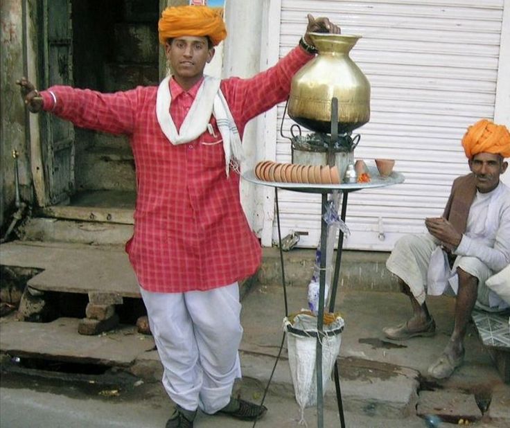 a man in an orange turban standing next to a table with a pot on it