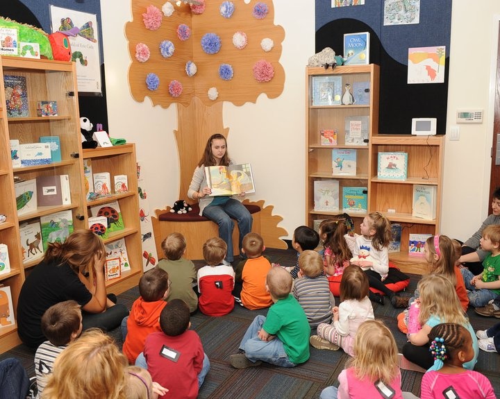 a group of children sitting on the floor in front of bookshelves with their teacher