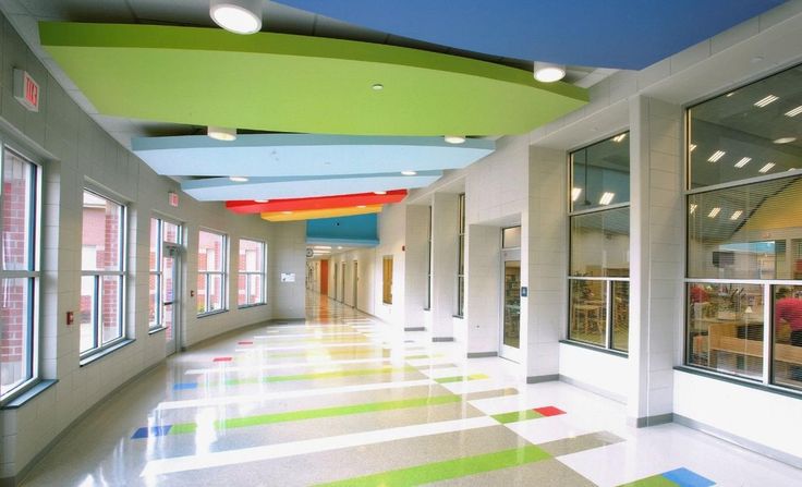 an empty hallway with multicolored flooring and large windows in the center is lit by brightly colored lights